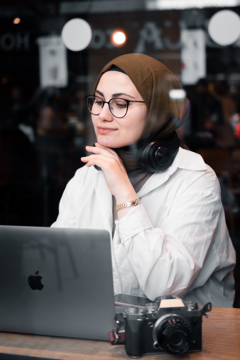 Businesswoman multitasking with a laptop and camera, working indoors.
