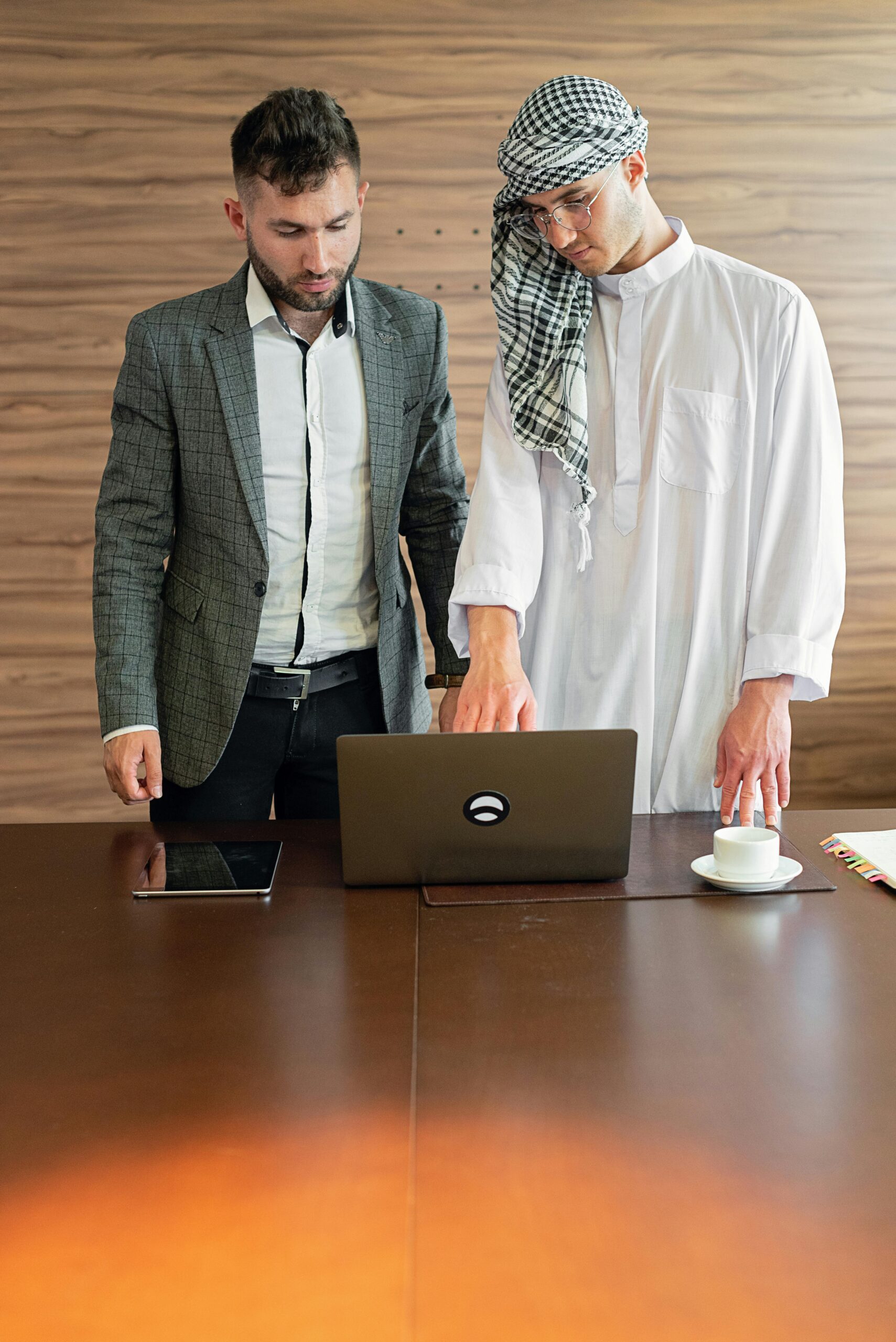 Two businessmen in traditional and modern attire working together on a laptop indoors.